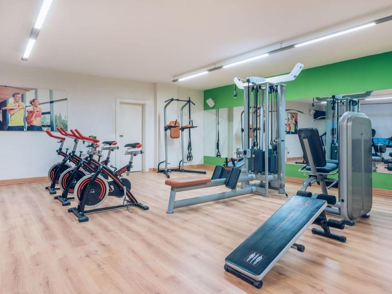 Gimnasio moderno con bicicletas, pesas y máquinas de entrenamiento sobre suelo de madera clara.