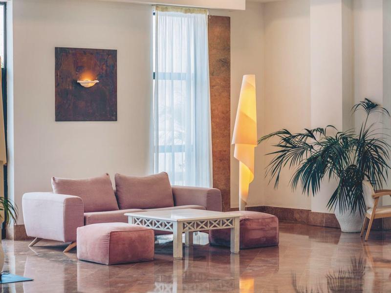 Cómodo rincón con sofá rosa, mesa de cristal y plantas en una habitación de hotel moderna.