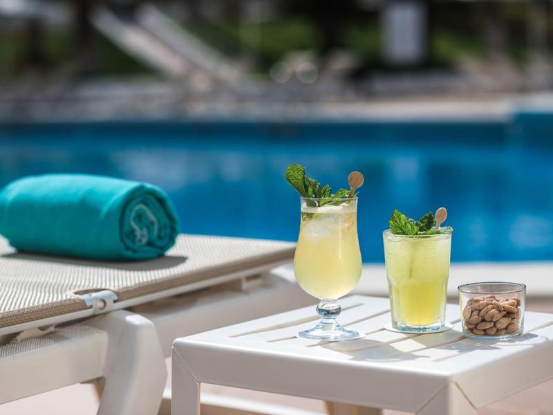 Dos cócteles refrescantes sobre una mesa blanca junto a tumbonas y piscina.