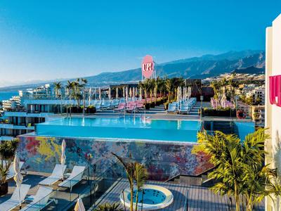 Moderní hotelový bazén s nekonečným okrajem, palmami, horami a mořem v pozadí.