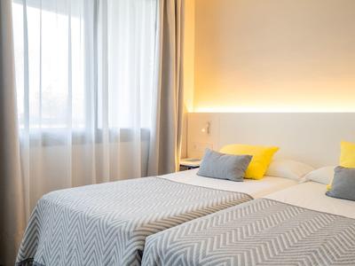 Dvoulůžkový pokoj se dvěma postelemi, jemným osvětlením a závěsy na okně.