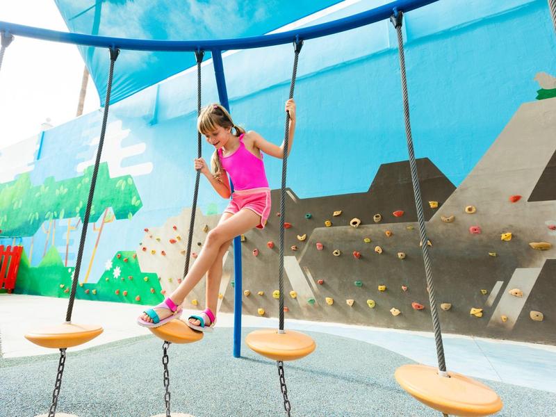 Dítě šplhá po zavěšených stupních v barevném vnitřním hřišti.