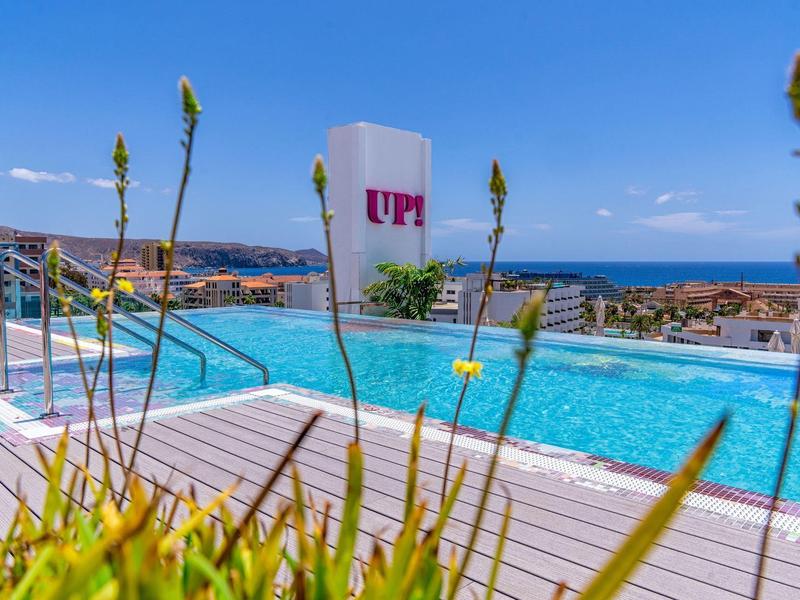 Moderní bazén s výhledem na moře a sluneční terasou za slunečného dne.