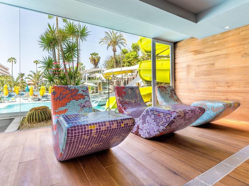 Moderní, barevná lehátka na dřevěné terase vedle bazénu s palmami.