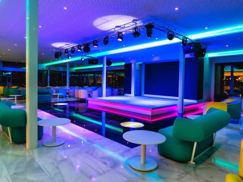 Moderní hotelový bar s barevným LED osvětlením a stylovými posezeními.