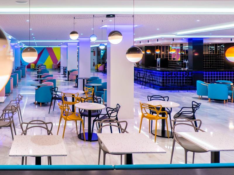 Moderní, světlý hotelový lounge s barevnými židlemi, stoly a závěsnými světly.