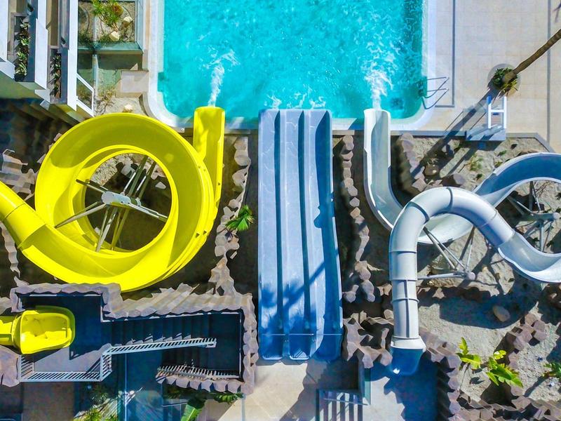 Letecký pohled na bazén s žlutými a modrými tobogány v hotelu nebo resortu.