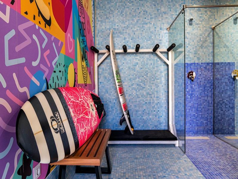 Barevná posilovna s běžeckým pásem, sprchami a pestrobarevným surfovým prknem v moderním prostředí.