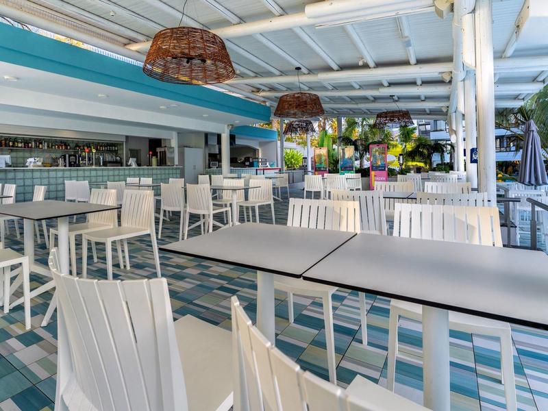 Moderní, světlá terasová restaurace s bílými židlemi a stolky pod zastřešenou částí.