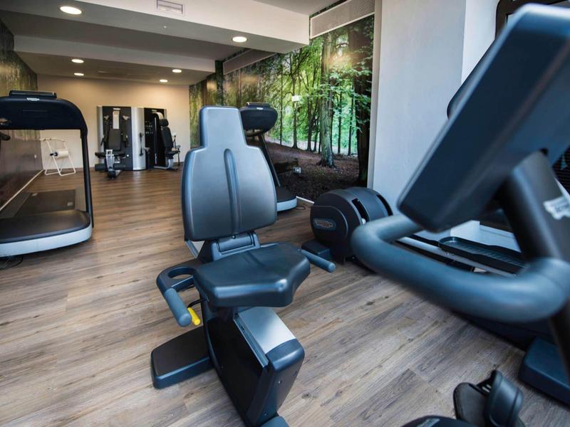Moderní posilovna se cvičebními stroji a dřevěnou podlahou v hotelu.