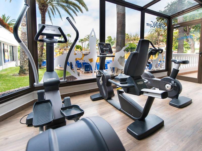 Moderní posilovna s kardio vybavením a velkými okny s výhledem na zahradu.