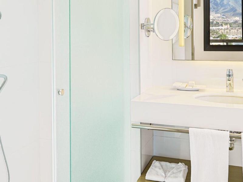 Čistá, moderní hotelová koupelna se sprchovým koutem, velkým zrcadlem a umyvadlem.