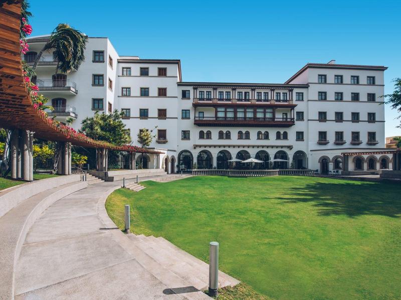 Edificio de hotel blanco con balcón y césped verde bajo cielo azul claro.