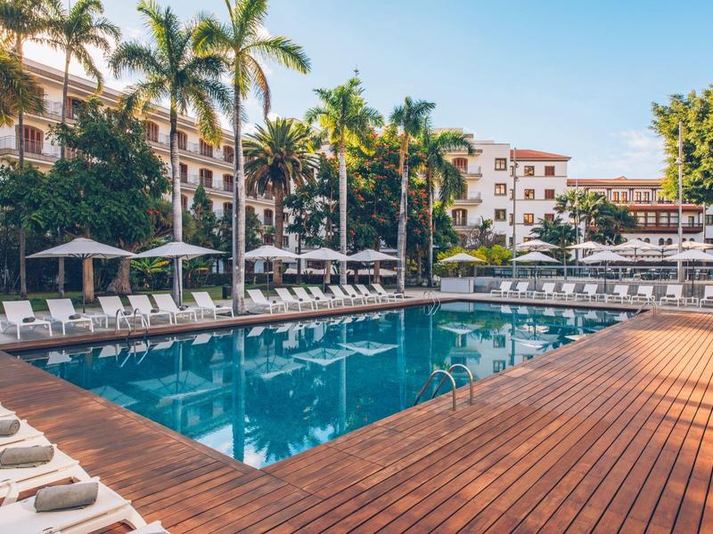 Gran piscina de hotel con tumbonas y palmeras bajo cielo despejado.