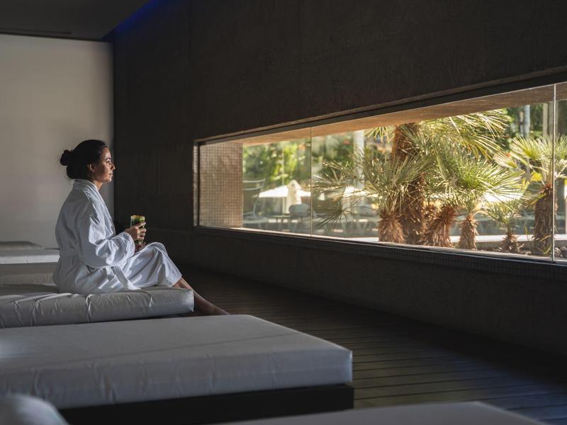 Persona sentada relajada en un salón moderno con vista a palmeras afuera.