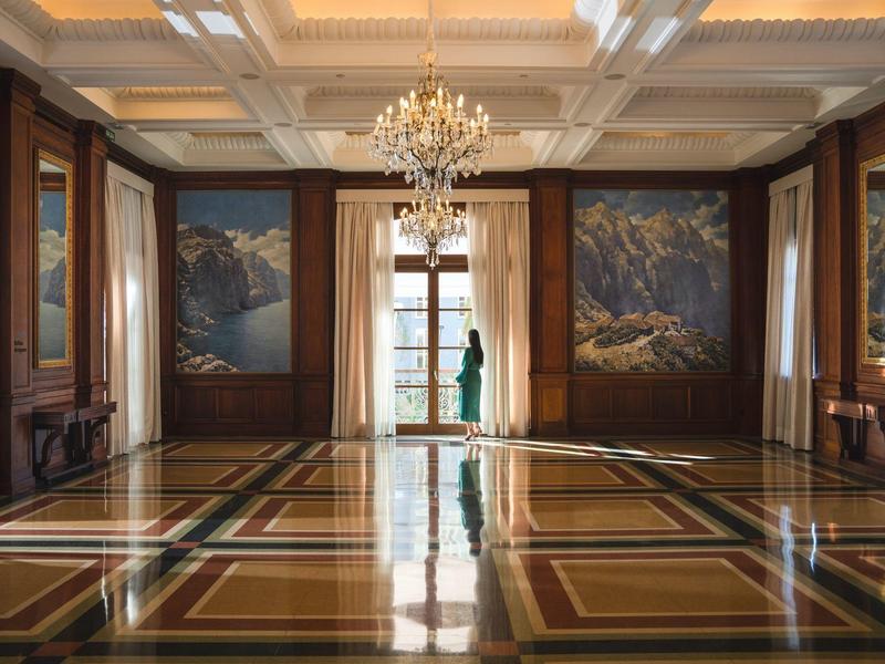 Amplio salón lujoso con suelo de mármol brillante, candelabro y pinturas de paisaje en las paredes.