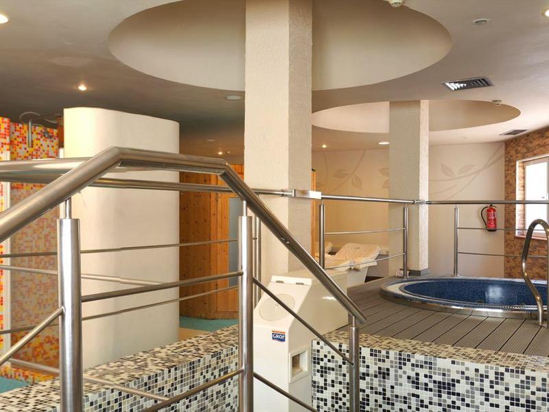 Área de bienestar moderna con jacuzzi, piso de baldosas y barandillas de acero inoxidable en habitación luminosa.