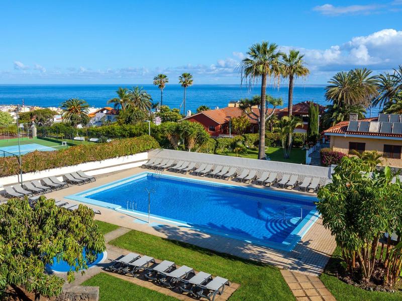Piscina exterior grande con tumbonas y palmeras en un hotel con vista al mar.