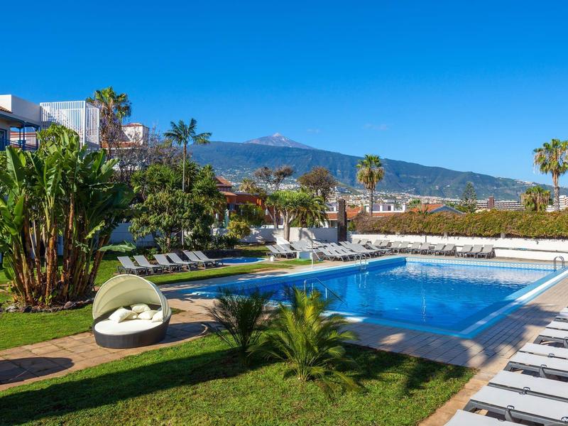 Piscina moderna del hotel con tumbonas y montañas al fondo bajo cielo despejado.