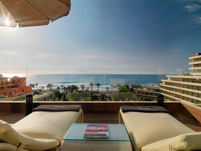 Deux chaises longues sur un balcon avec vue sur une plage et l'océan sous un ciel bleu.