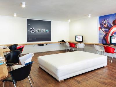 Salle de jeux moderne avec plusieurs consoles, ottomane blanche et chaises colorées sur sol en bois