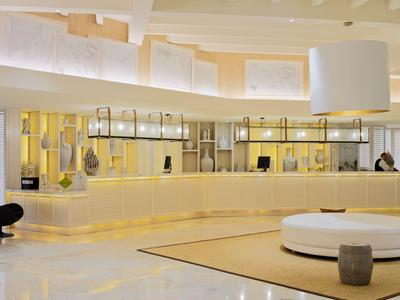 Heller Hotel-Lobbybereich mit hellem Empfangstresen, modernen Sitzgelegenheiten und großem, rundem Teppich.