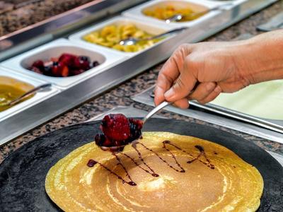 Main versant de la sauce au chocolat sur une crêpe avec des fruits dans un buffet.