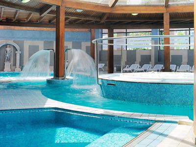 Espace piscine intérieure avec eau claire, chaises longues et fontaines sous un toit en bois.