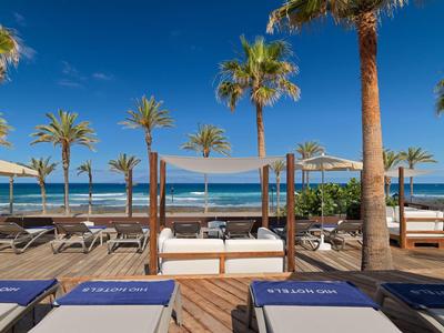 Station balnéaire de luxe avec palmiers, chaises longues et parasols au bord de l'océan.
