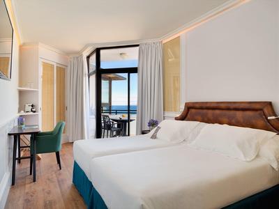 Chambre d'hôtel avec grand lit, bureau et balcon avec vue sur la mer.