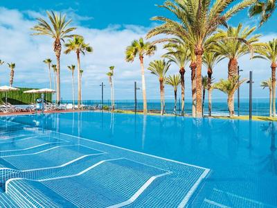Piscine bleue claire avec des palmiers sous un ciel lumineux, idéale pour la détente tropicale.