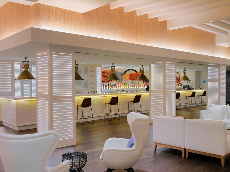 Hall d'hôtel moderne avec un bar élégant, fauteuils blancs et éclairage chaleureux.