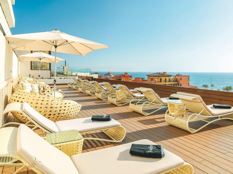 Terrasse d'hôtel ensoleillée avec transats et parasols face à la mer.