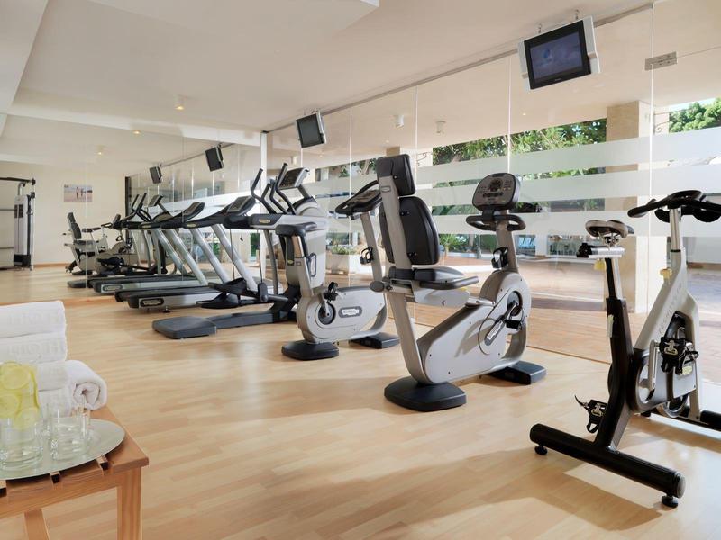 Salle de sport lumineuse avec appareils cardio et grandes fenêtres donnant sur la verdure.