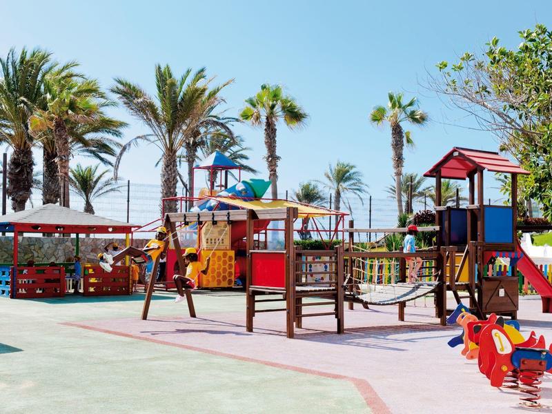 Aire de jeux colorée avec toboggans et structures d'escalade près des palmiers par une journée ensoleillée.