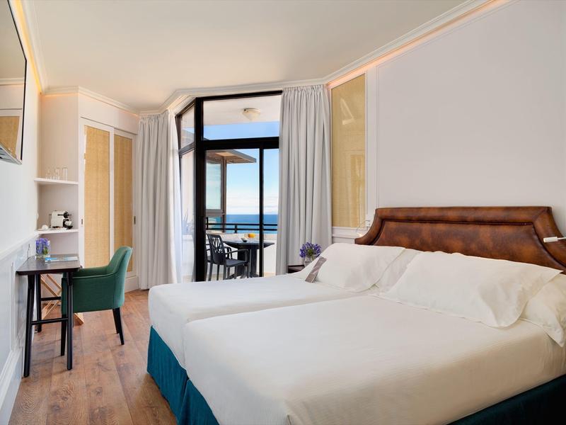 Chambre d'hôtel avec grand lit, bureau et balcon avec vue sur la mer.