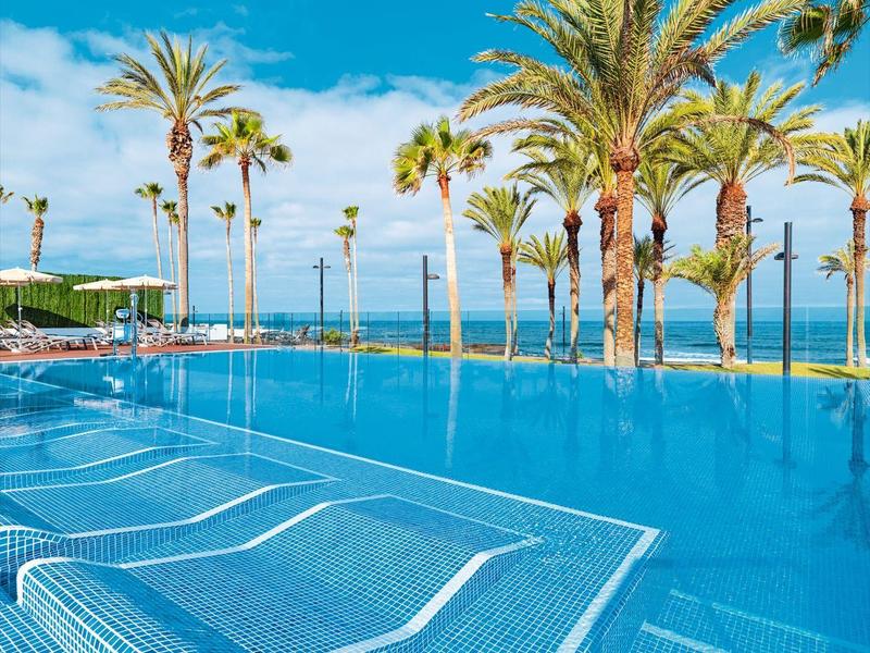 Piscine bleue claire avec des palmiers sous un ciel lumineux, idéale pour la détente tropicale.