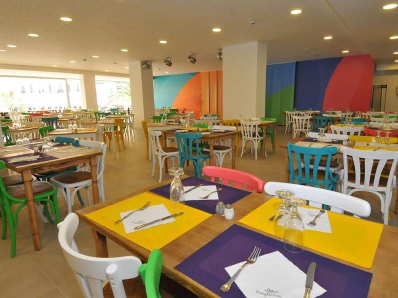 Moderner, bunter Speisesaal mit rechteckigen Tischen und gemischten Stühlen aus Holz und Kunststoff.