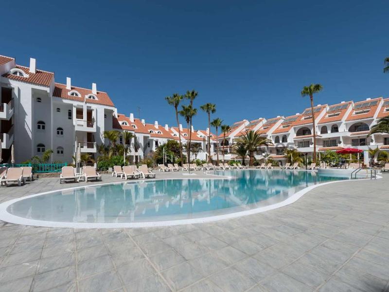 Moderne mehrstöckige Wohnhäuser mit roten Dächern und Palmen um einen großen, runden Außenpool.