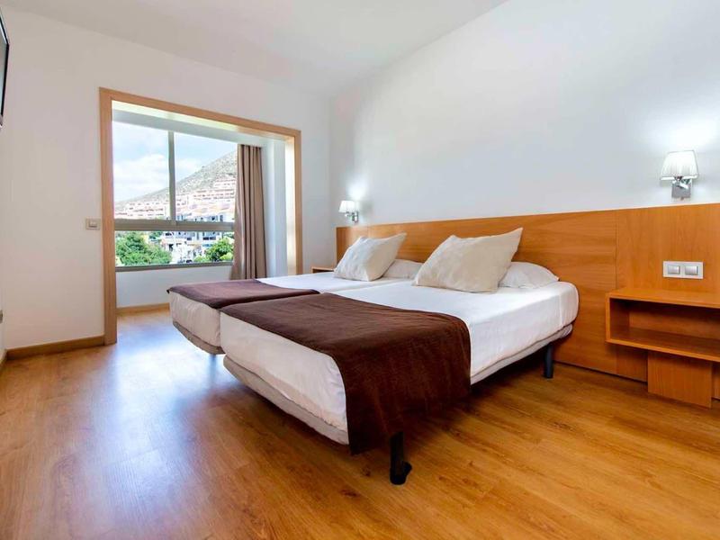 Helles Schlafzimmer mit Holzboden, Doppelbett, weißen Wänden und Balkon mit Bergblick.