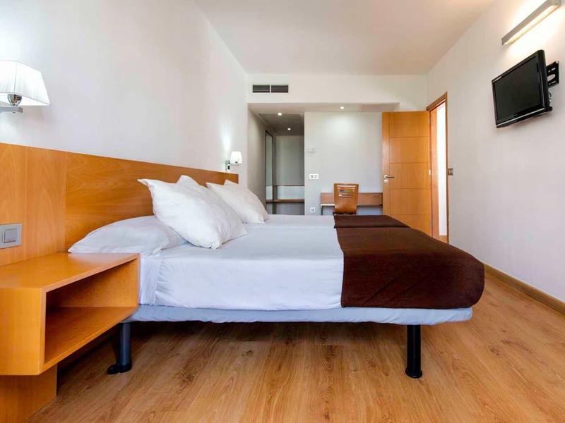 Moderner Hotelzimmer mit Doppelbett, Holzfußboden, Wand-TV und minimalistischer Einrichtung.