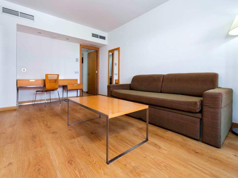 Moderner Wohnraum mit braunem Sofa, Holz-Tisch, Schreibtisch, Stuhl und heller Wandbeleuchtung.