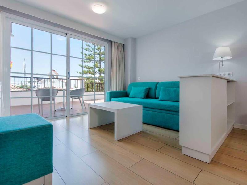 Helles Wohnzimmer mit hellblauem Sofa, weißem Tisch, Holzboden und Balkon mit Stadtblick.