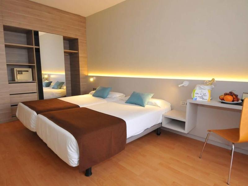 Hotelzimmer mit Doppelbett, braunen Decken, Schreibtisch, Stuhl und offenem Kleiderschrank.