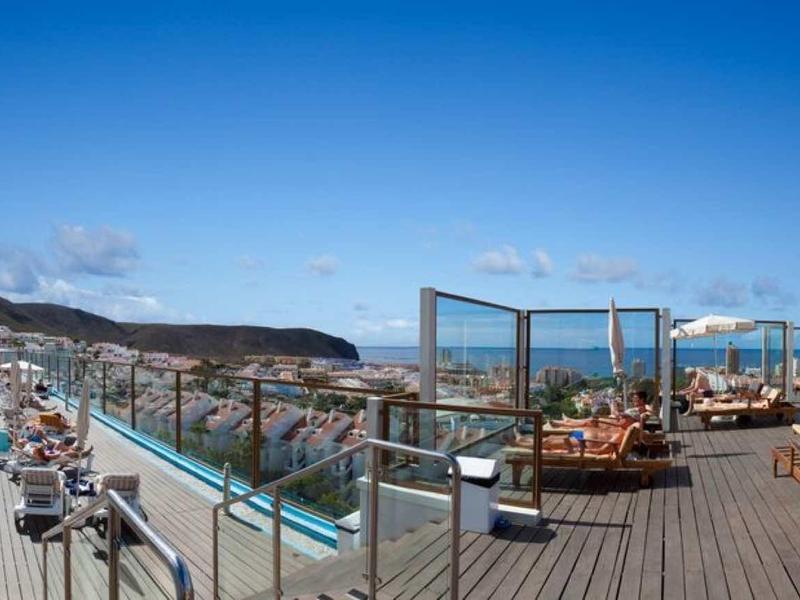 Große Terrasse mit Liegestühlen, Sonnenschirmen und Blick auf Hügel bei klarem Himmel.