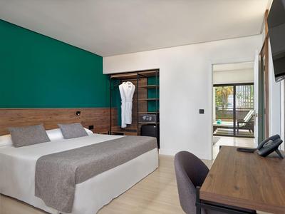 Camera d'hotel moderna con letto matrimoniale, cuscini grigi, scrivania in legno e armadio aperto.