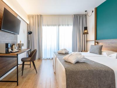 Camera d'hotel moderna con letto matrimoniale, TV, scrivania e ampia finestra luminosa.