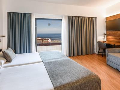 Camera d'hotel moderna con letti matrimoniali e finestra grande con vista mare.