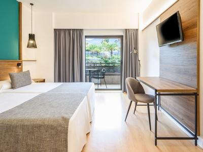 Camera d'hotel moderna con letto matrimoniale, scrivania, TV a parete e balcone con vista.