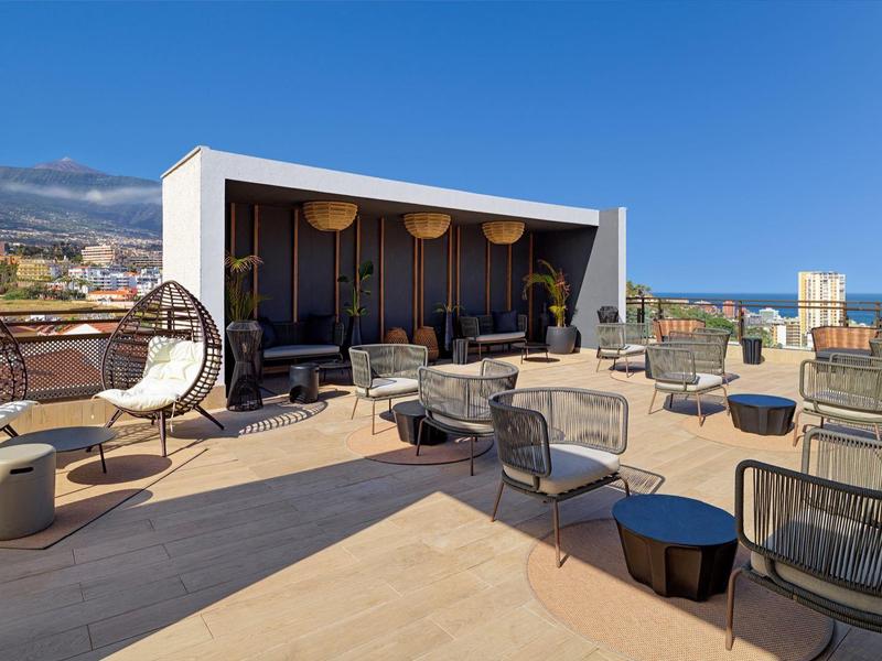 Terrazza di un hotel moderno con sedie comode e vista urbana sotto un cielo sereno.